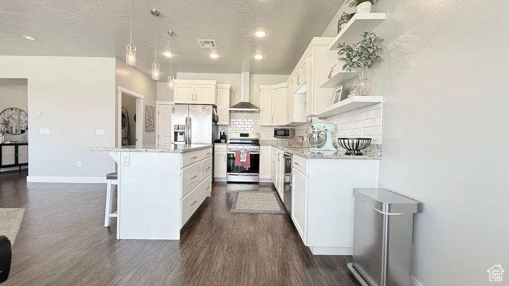 Kitchen featuring appliances with stainless steel finishes, a kitchen bar, a kitchen island, dark wood-style floors, and open shelves