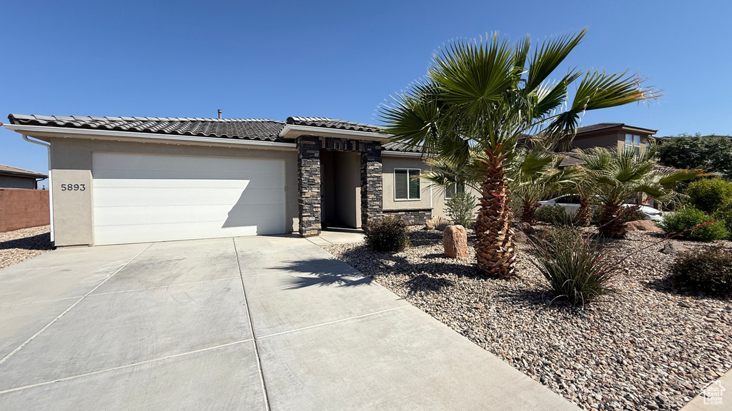 View of front of house featuring driveway, an attached garage, stucco siding, a tile roof, and stone siding