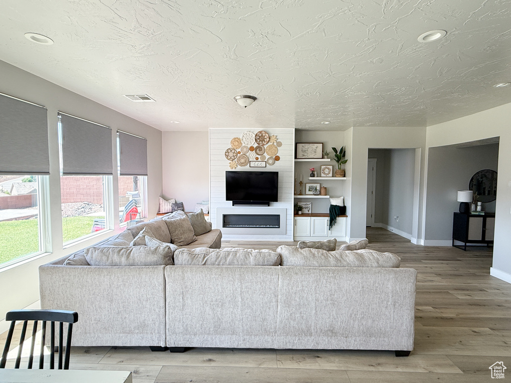 Living room with a textured ceiling, light wood-style floors, recessed lighting, and a glass covered fireplace