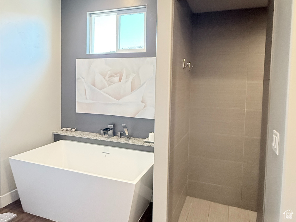 Bathroom featuring wood finished floors, a soaking tub, a tile shower, baseboards, and a textured ceiling