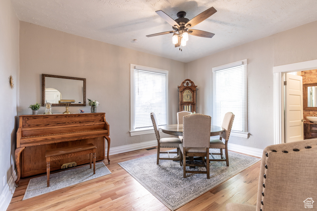 Dining space with baseboards, a ceiling fan, light wood-style floors, and a textured ceiling