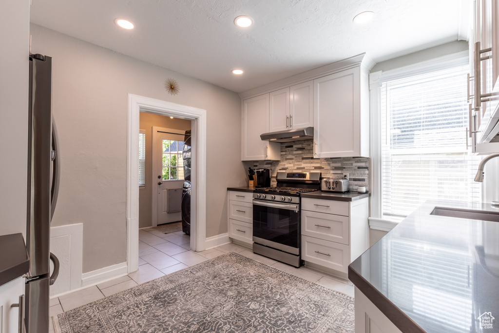 Kitchen with stainless steel appliances, under cabinet range hood, a sink, decorative backsplash, and dark countertops