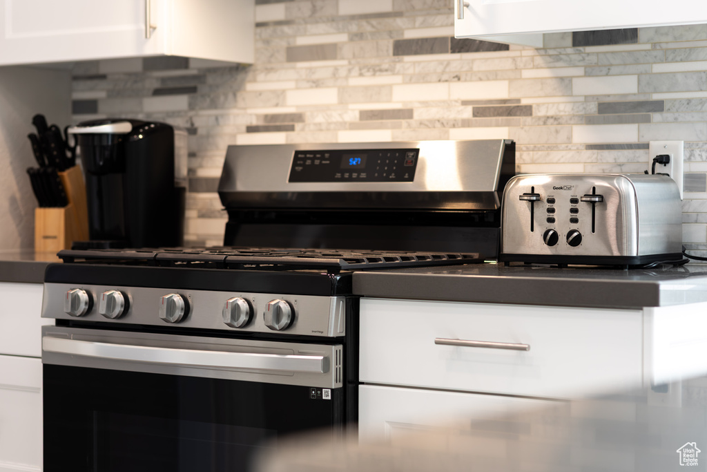 Kitchen with stainless steel gas stove, decorative backsplash, dark countertops, and white cabinets