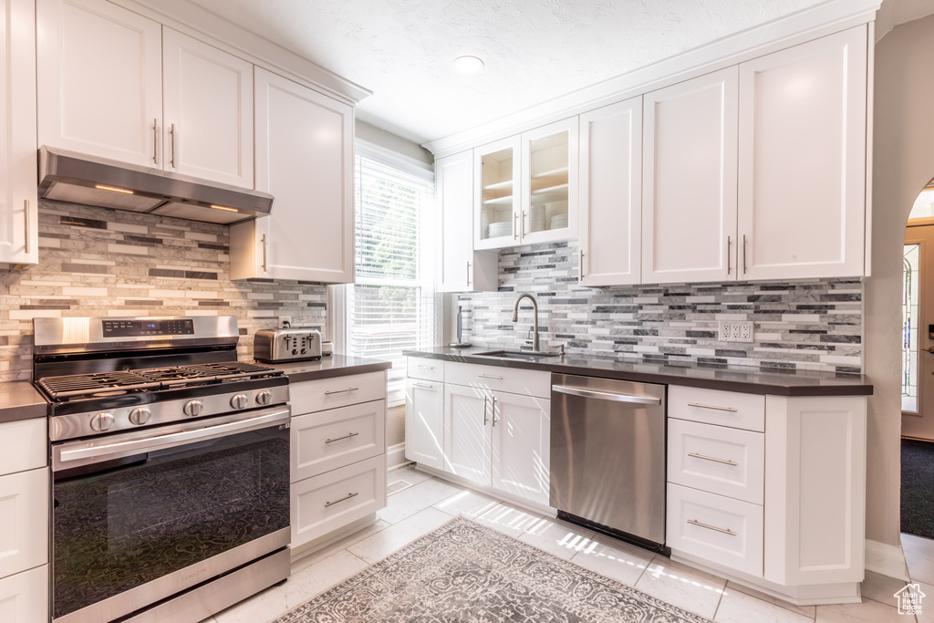 Kitchen with stainless steel appliances, under cabinet range hood, a sink, dark countertops, and light tile patterned floors