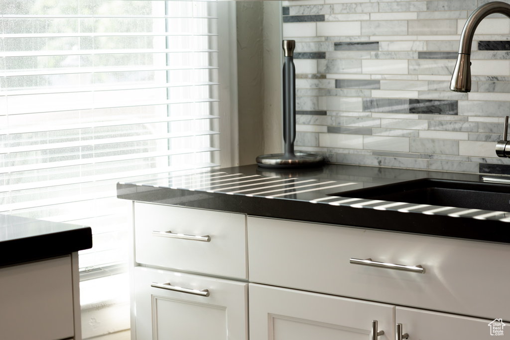 Kitchen view of backsplash, white cabinets, and dark countertops