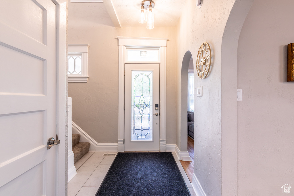 Foyer entrance with arched walkways, light tile patterned floors, stairs, and a textured wall
