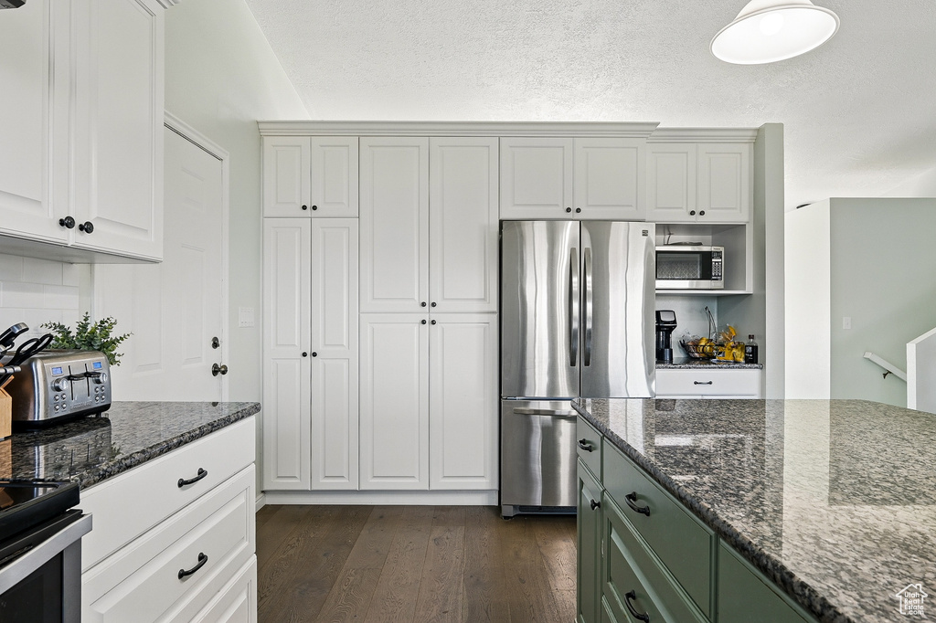 Kitchen with stainless steel appliances, dark wood-style flooring, dark stone counters, and white cabinets