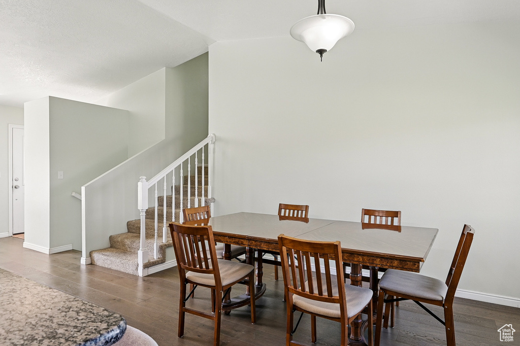 Dining room featuring dark wood-style flooring, stairway, baseboards, and vaulted ceiling