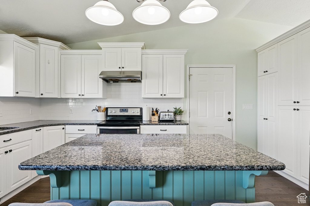 Kitchen with electric range, under cabinet range hood, lofted ceiling, a kitchen breakfast bar, and backsplash