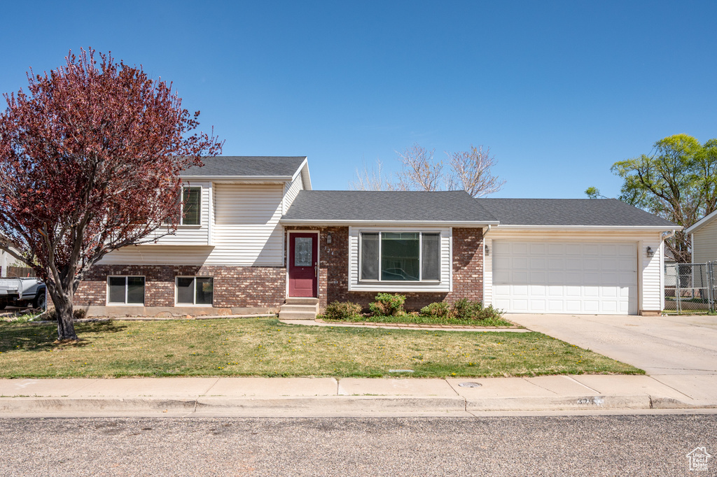 Split level home with brick siding, an attached garage, driveway, and entry steps