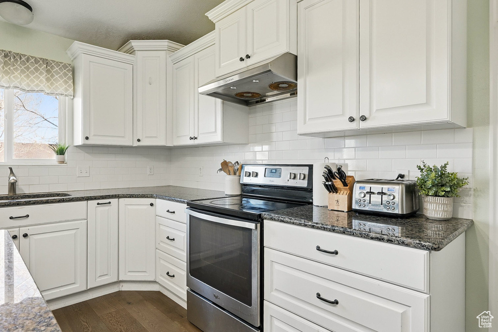Kitchen with electric stove, under cabinet range hood, a sink, white cabinets, and backsplash