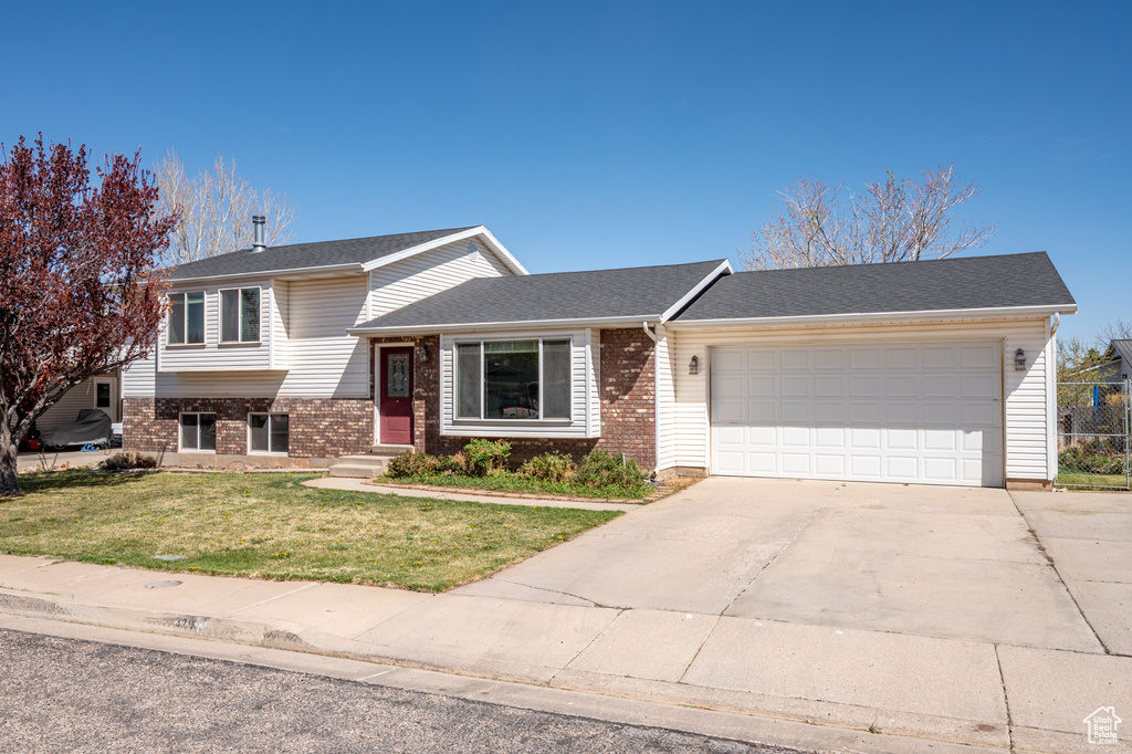 Split level home featuring a garage, a front yard, concrete driveway, brick siding, and a shingled roof