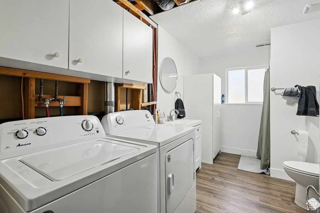 Laundry area featuring washer and dryer, light wood-style flooring, baseboards, and a textured ceiling