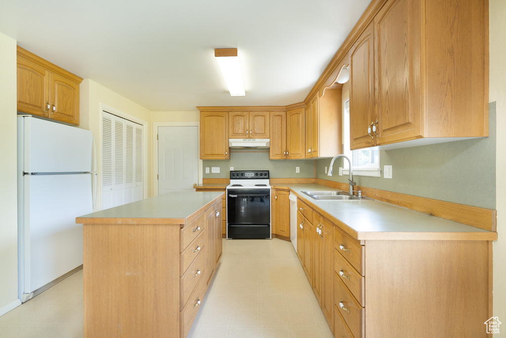 Kitchen with range with electric cooktop, freestanding refrigerator, a sink, under cabinet range hood, and a kitchen island