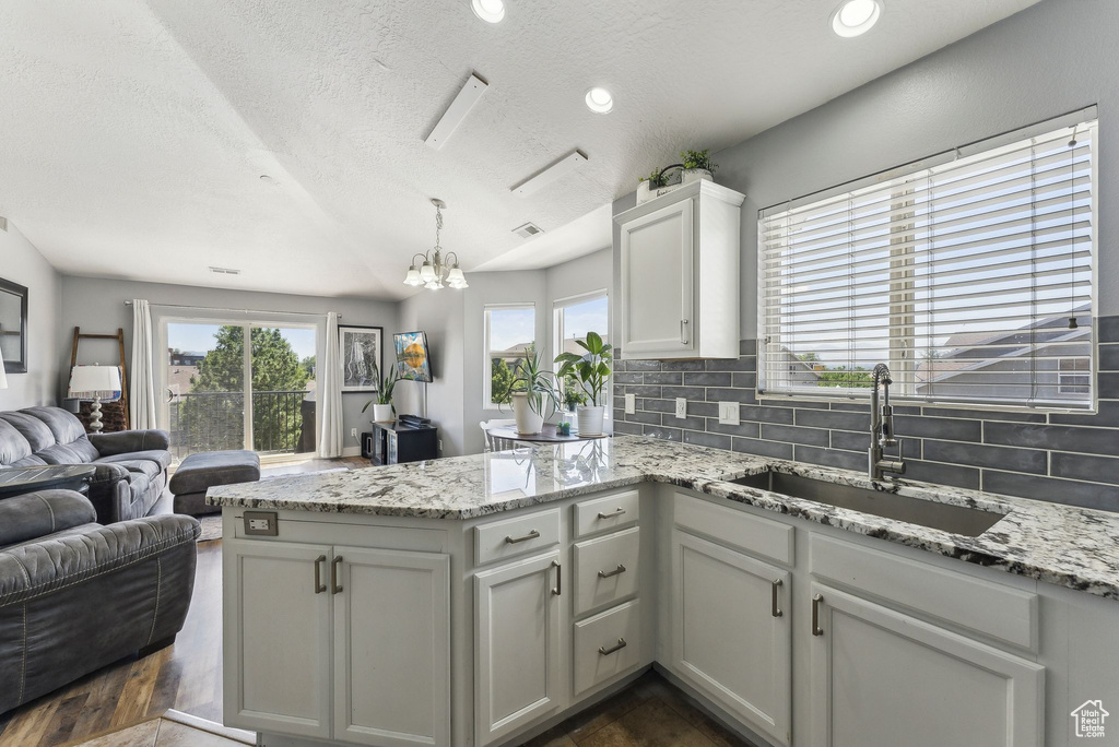 Kitchen with a sink, a peninsula, open floor plan, decorative backsplash, and a chandelier
