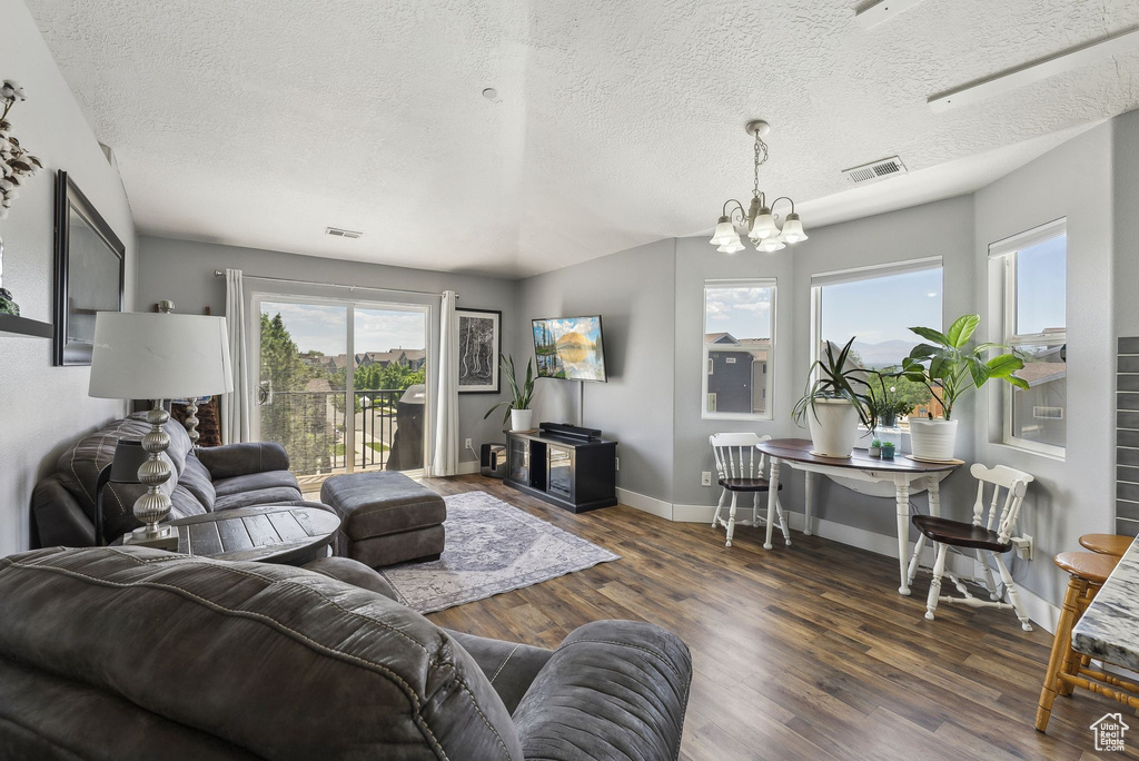 Living area with a chandelier, wood finished floors, plenty of natural light, baseboards, and a textured ceiling