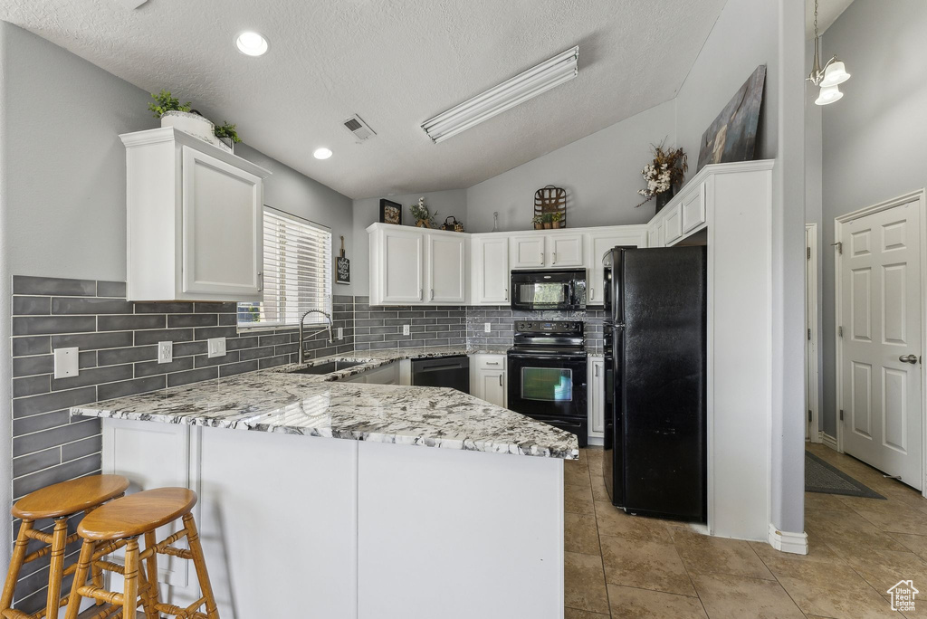 Kitchen featuring black appliances, a sink, a peninsula, white cabinets, and light stone countertops
