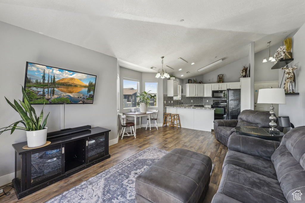 Living area with a chandelier, a textured ceiling, dark wood-type flooring, lofted ceiling, and baseboards