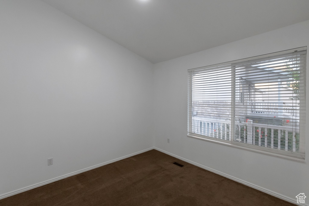 Unfurnished room featuring dark carpet, lofted ceiling, and baseboards