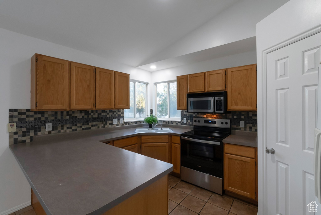 Kitchen with stainless steel appliances, a peninsula, a sink, vaulted ceiling, and tasteful backsplash