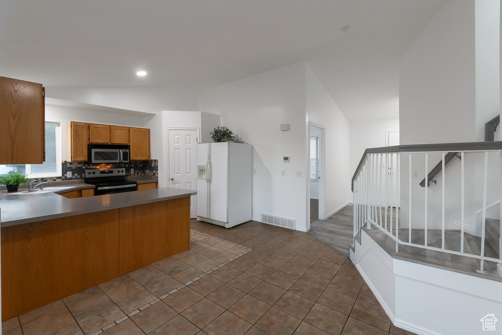 Kitchen with stainless steel appliances, vaulted ceiling, brown cabinets, a peninsula, and backsplash