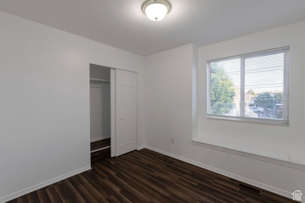 Unfurnished bedroom featuring dark wood-type flooring, baseboards, and a closet