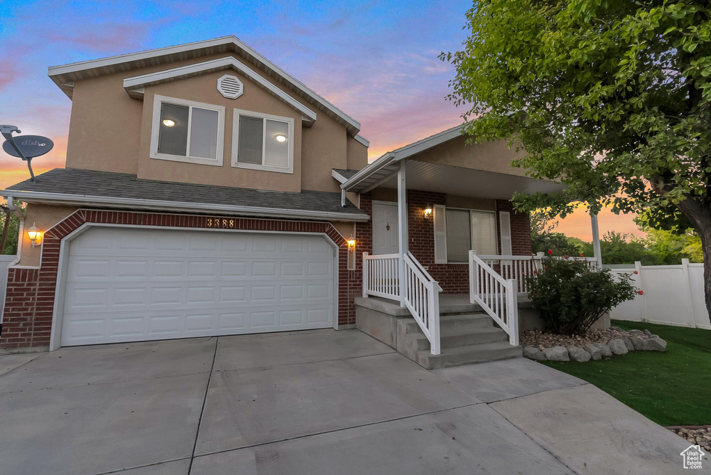 View of front facade featuring brick siding, an attached garage, concrete driveway, stucco siding, and covered porch