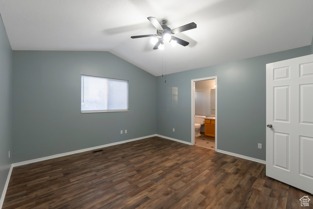 Unfurnished bedroom featuring dark wood-style flooring, vaulted ceiling, baseboards, a ceiling fan, and ensuite bath