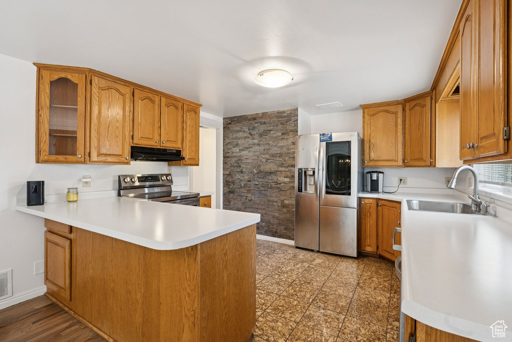 Kitchen featuring appliances with stainless steel finishes, a sink, under cabinet range hood, a peninsula, and brown cabinetry