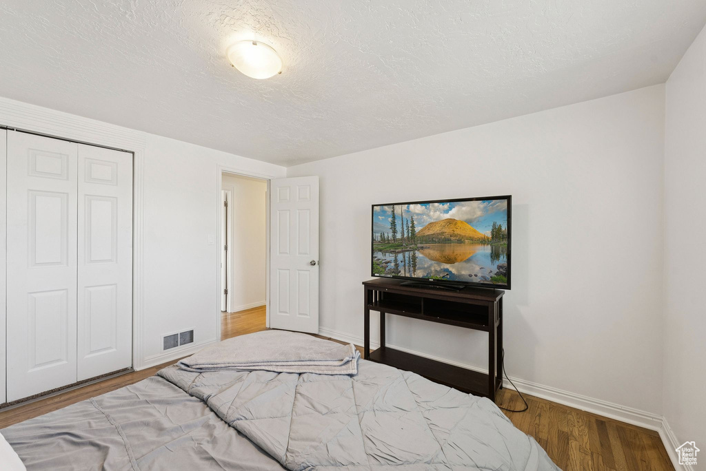 Bedroom featuring baseboards, wood finished floors, a closet, and a textured ceiling