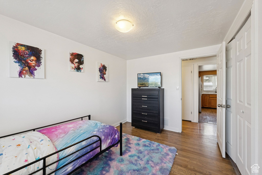 Bedroom with wood finished floors, a closet, baseboards, and a textured ceiling