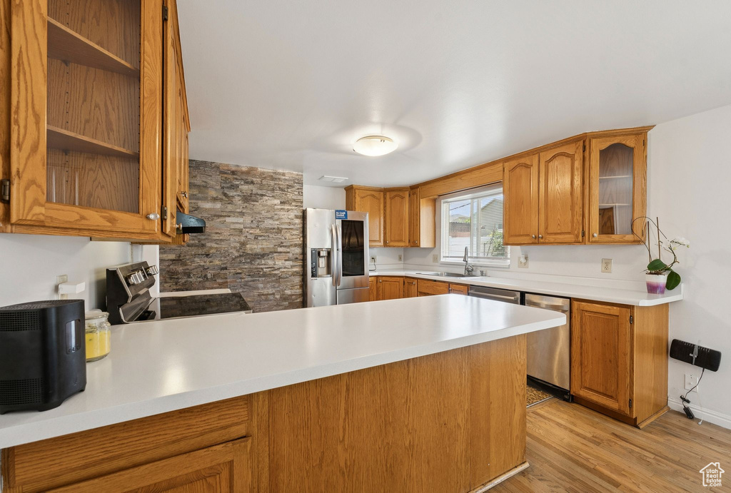 Kitchen with stainless steel appliances, a sink, a peninsula, glass insert cabinets, and light countertops