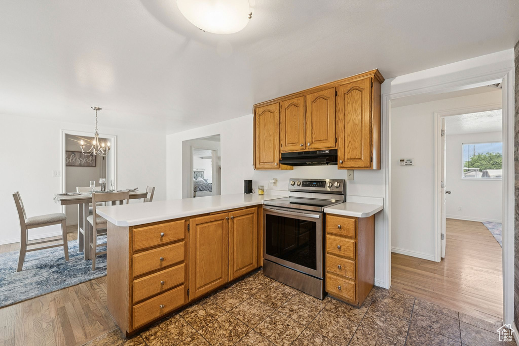 Kitchen with under cabinet range hood, stainless steel electric stove, a chandelier, and light countertops