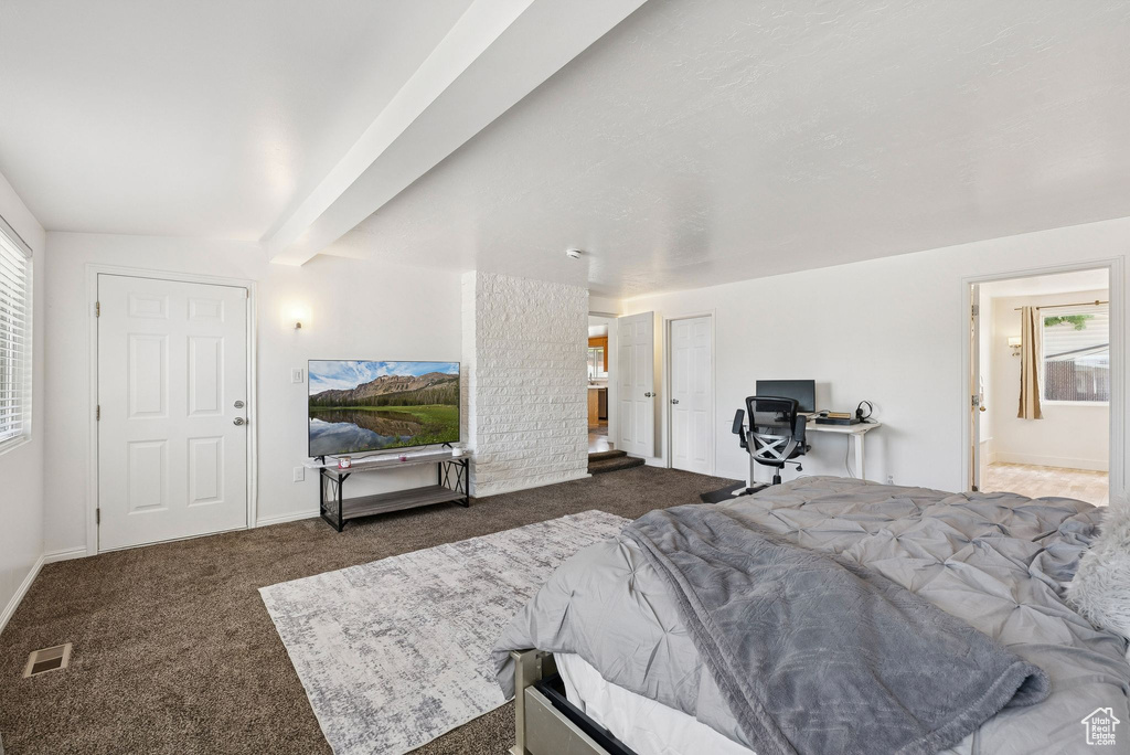 Carpeted bedroom with multiple windows, beamed ceiling, baseboards, and connected bathroom
