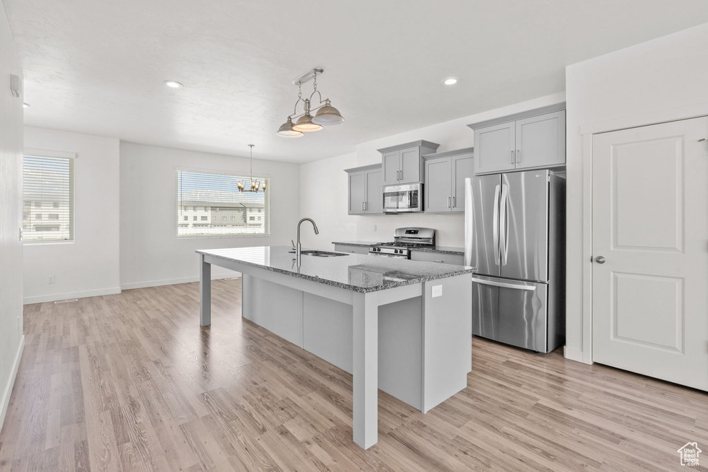 Kitchen featuring appliances with stainless steel finishes, gray cabinetry, a sink, light stone countertops, and a center island with sink