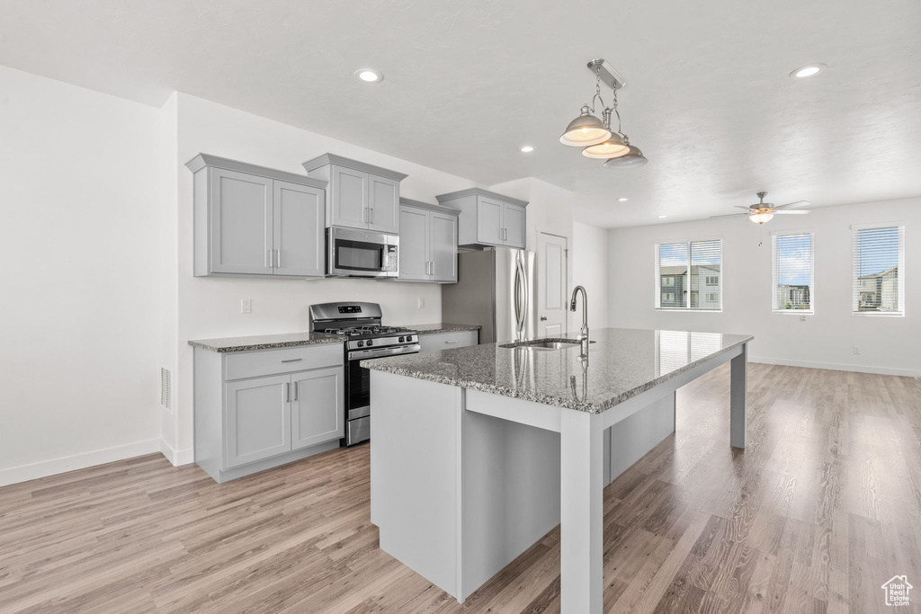 Kitchen with appliances with stainless steel finishes, gray cabinets, a sink, a breakfast bar, and light wood finished floors