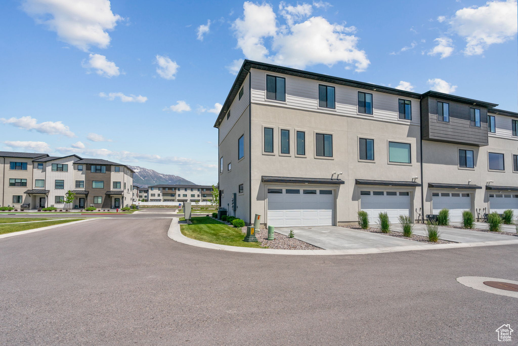 View of building exterior featuring an attached garage, a residential view, concrete driveway, and a mountain view