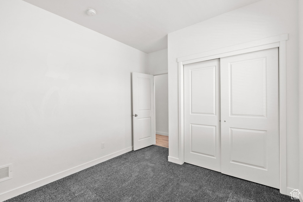 Unfurnished bedroom featuring dark colored carpet, baseboards, and a closet