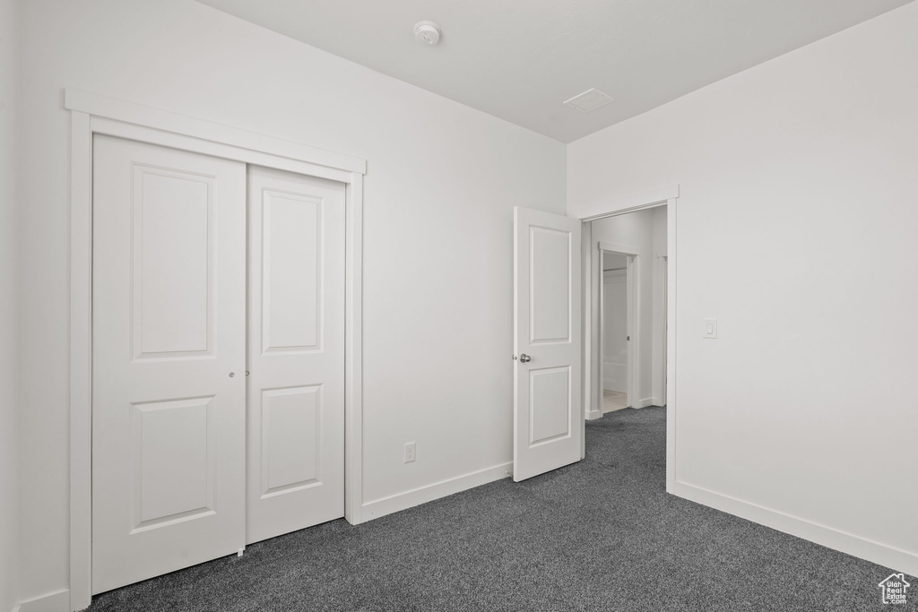 Unfurnished bedroom with dark colored carpet, baseboards, and a closet