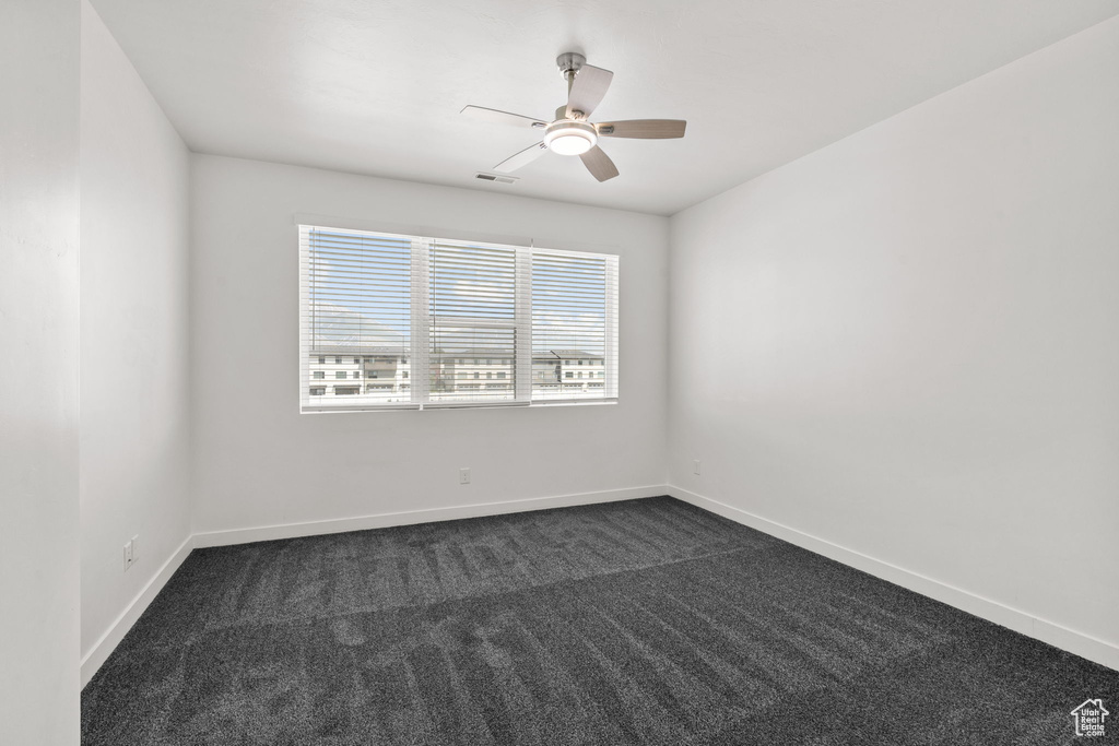 Empty room featuring dark carpet, ceiling fan, and baseboards