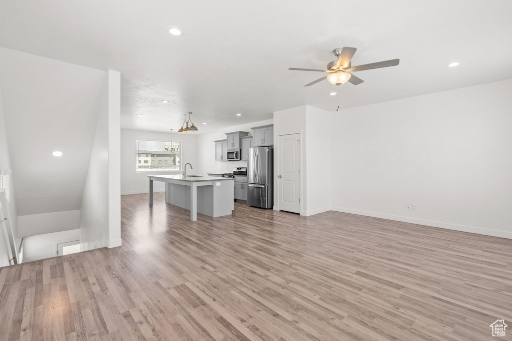 Unfurnished living room featuring ceiling fan, light wood-style flooring, recessed lighting, a chandelier, and a sink
