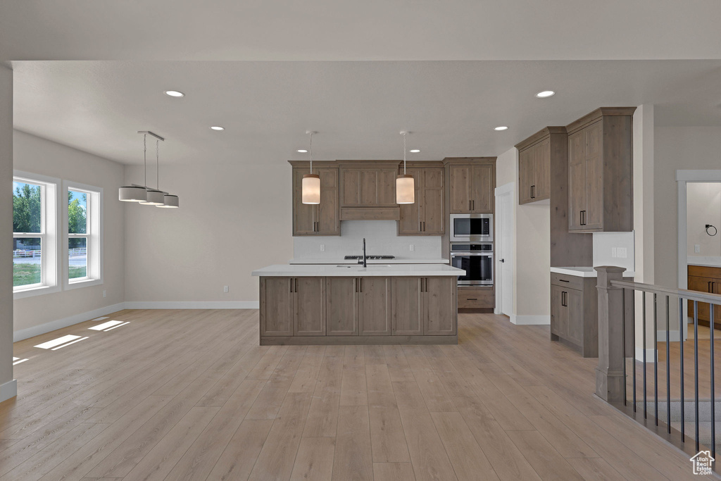 Kitchen featuring stainless steel appliances, light countertops, baseboards, light wood finished floors, and recessed lighting