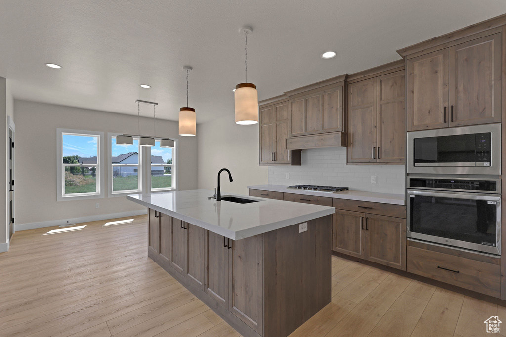 Kitchen featuring stainless steel appliances, a sink, light wood-style floors, light countertops, and a center island with sink