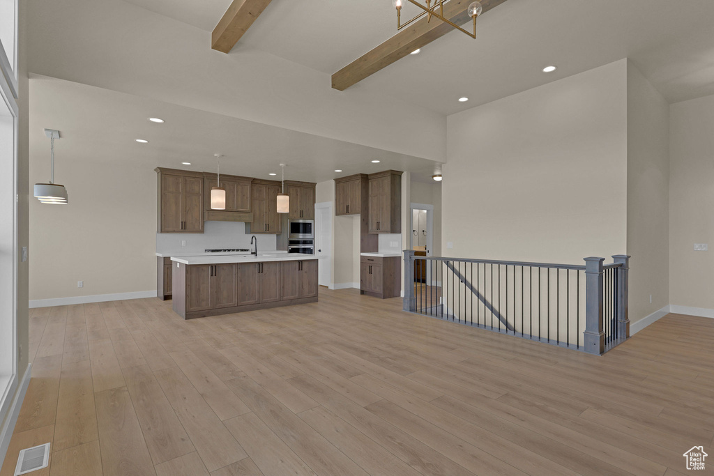 Unfurnished living room with beam ceiling, light wood-style floors, a sink, baseboards, and recessed lighting