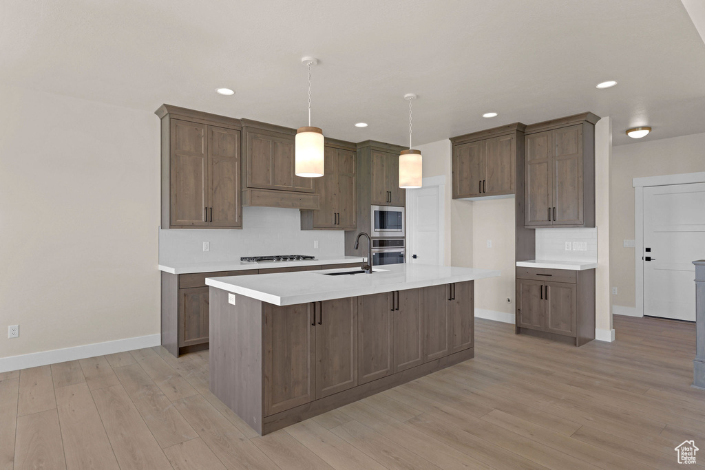 Kitchen featuring a sink, stainless steel appliances, baseboards, light wood finished floors, and recessed lighting