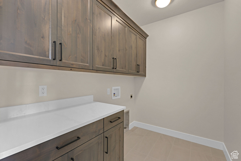 Washroom with hookup for an electric dryer, cabinet space, hookup for a washing machine, baseboards, and light tile patterned floors