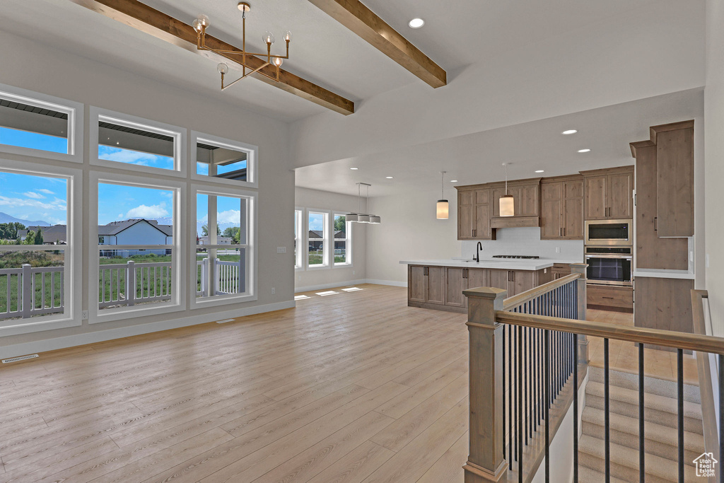 Kitchen featuring stainless steel appliances, open floor plan, beamed ceiling, light countertops, and light wood-type flooring
