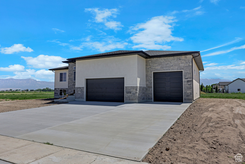 View of home\'s exterior with stone siding, a mountain view, driveway, a garage, and stucco siding