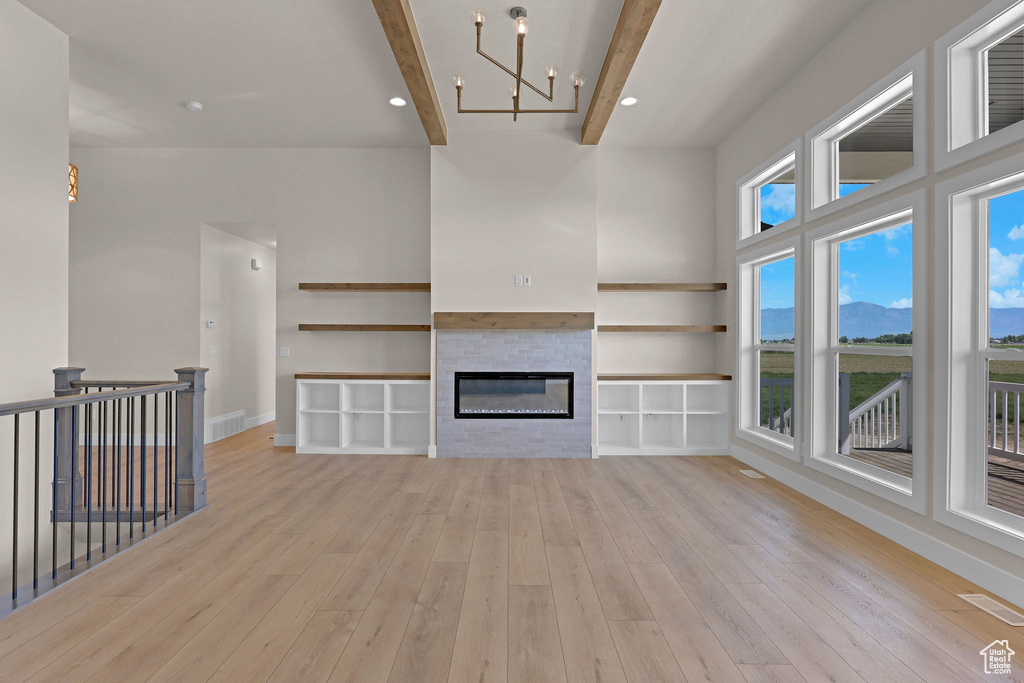 Unfurnished living room with beamed ceiling, light wood-type flooring, a chandelier, a glass covered fireplace, and a mountain view