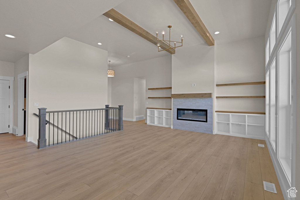 Unfurnished living room featuring light wood-type flooring, beamed ceiling, a chandelier, recessed lighting, and a glass covered fireplace